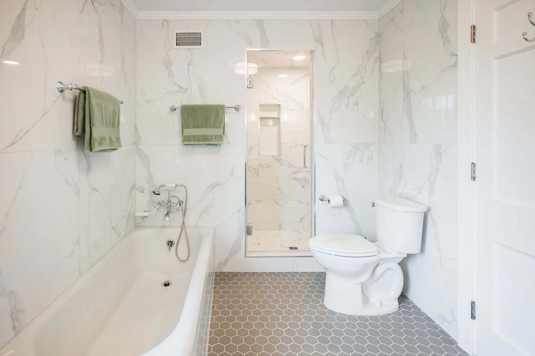 Completed bathroom remodel with marble-look wall tile, bathtub, glass shower, toilet, and gray hexagonal floor