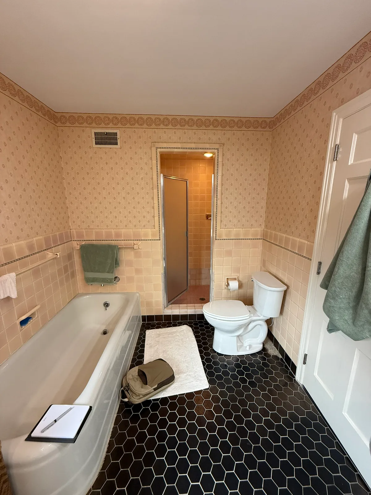 Bathroom before remodeling with pink tile, wallpaper, bathtub, shower, and black hexagonal floor