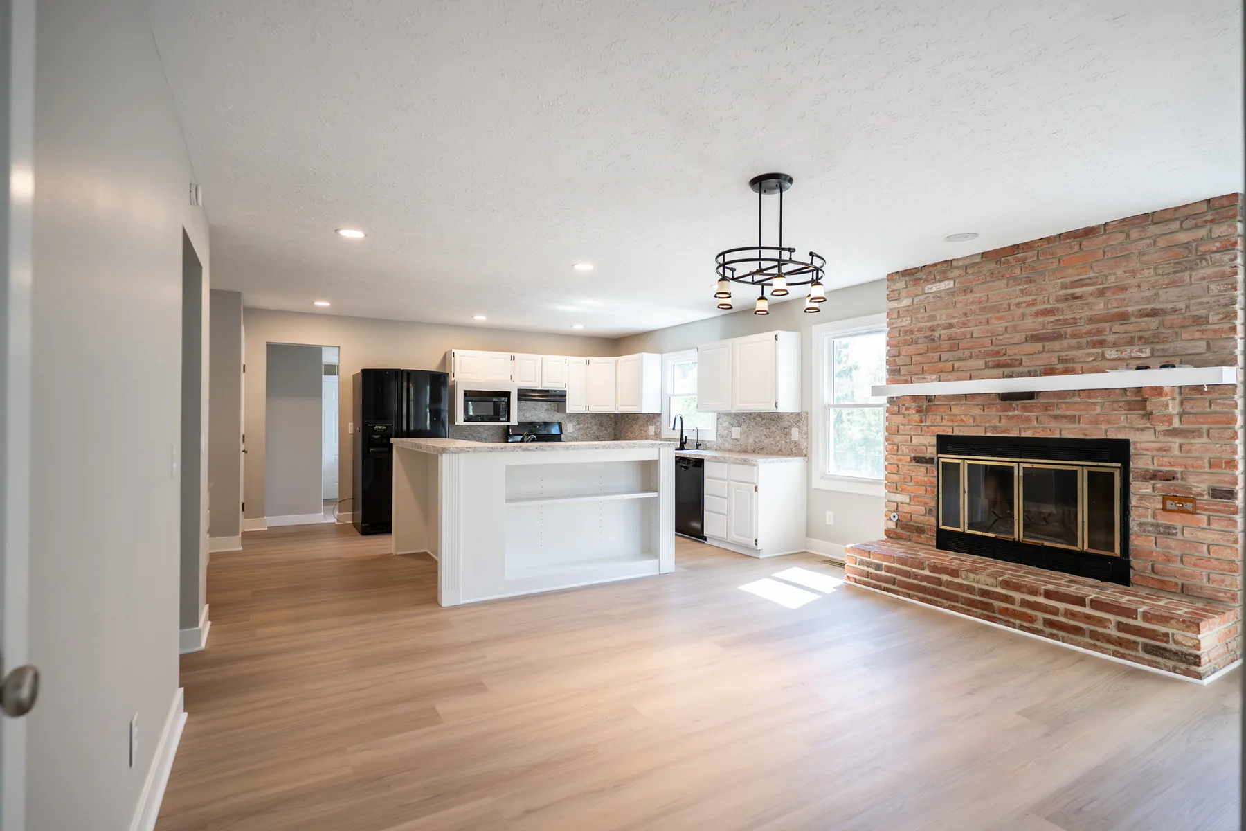 Renovated kitchen and fireplace area with white cabinets, light flooring, gray walls, and brick fireplace