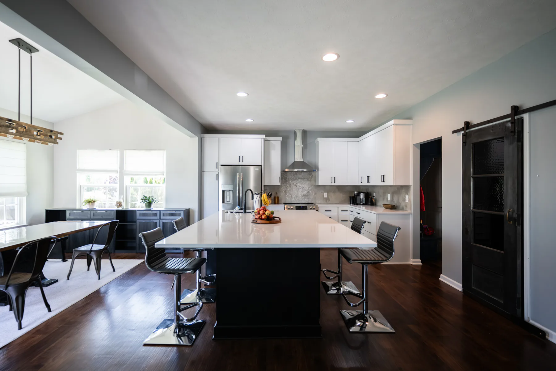 Completed kitchen remodel with white flat-panel cabinets, black island, white countertops, stainless appliances, and dark wood flooring